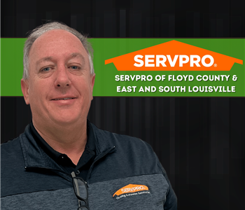  an smiling at camera with SERVPRO logo on wall and dark background 