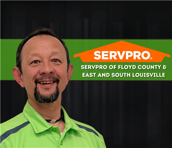 man smiling at camera with SERVPRO logo and dark coloring on wall